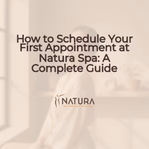 A woman with glowing skin, elegant posture, and a genuine confident smile is touching her face. The background is softly blurred with warm beige, cream, and soft brown tones, creating a luxurious and natural spa-like atmosphere.