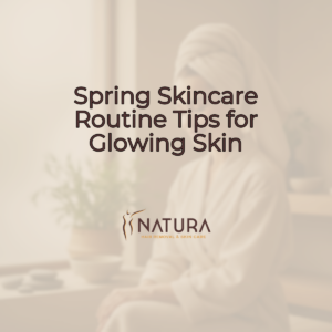 A woman with radiant skin, wearing a towel wrap in a spa setting, smiles confidently. The background is softly blurred with warm beige and brown tones.