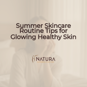 A woman with glowing skin, soft smile, and relaxed pose, set against a blurred warm beige/cream/soft brown background.