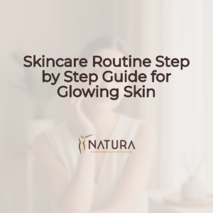 A woman with dewy complexion and a soft, confident smile, gently touching her face. The background is softly blurred with warm beiges and creams. She embodies a natural, luxurious skincare aesthetic.